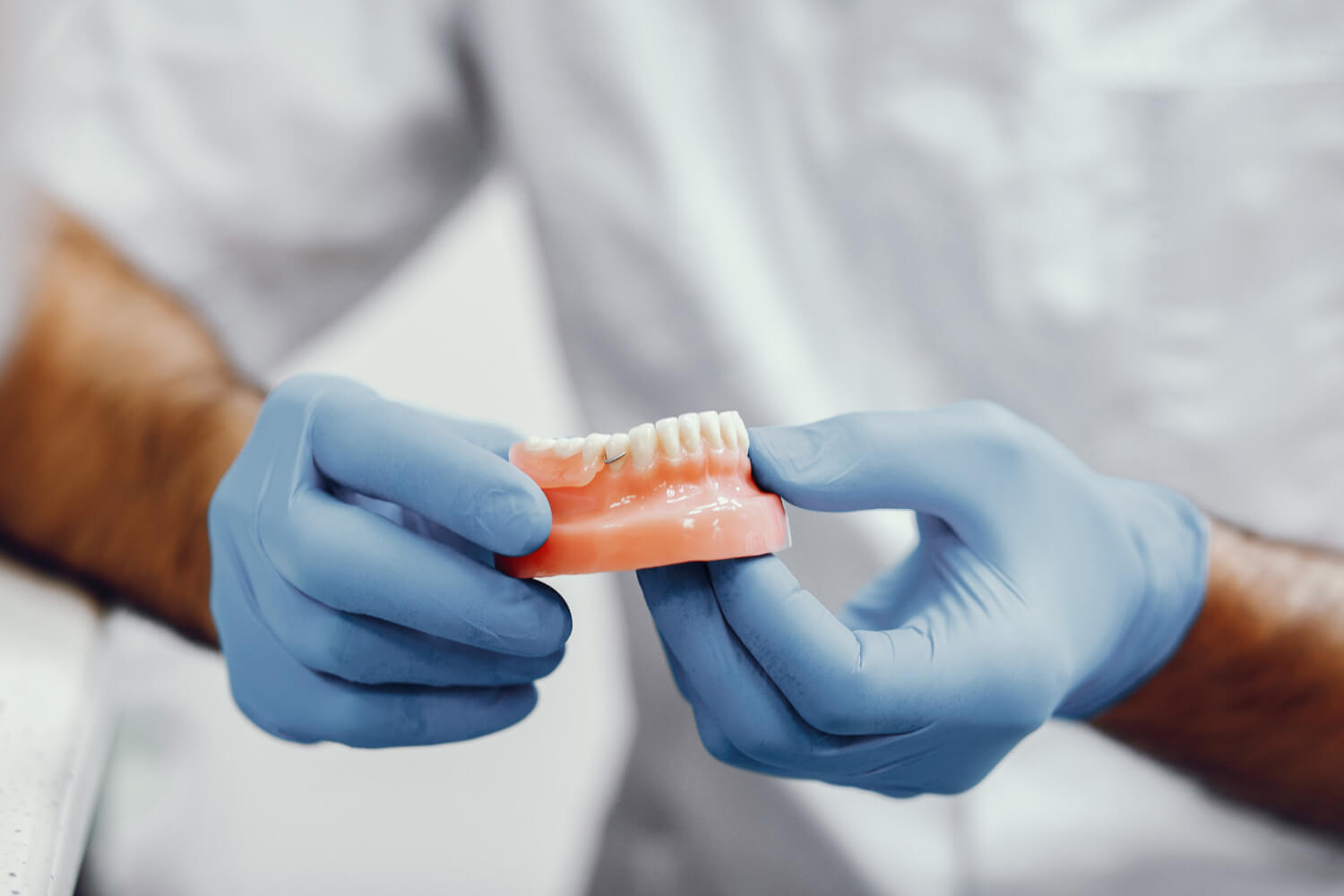 Dentista com luvas azuis segurando modelo de prótese para reabilitação oral na Smile Center, José Bonifácio, Zona Leste SP.