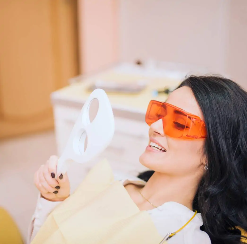 Paciente admirando novo sorriso com lentes de contato dental no espelho na Smile Center, José Bonifácio, Zona Leste SP.