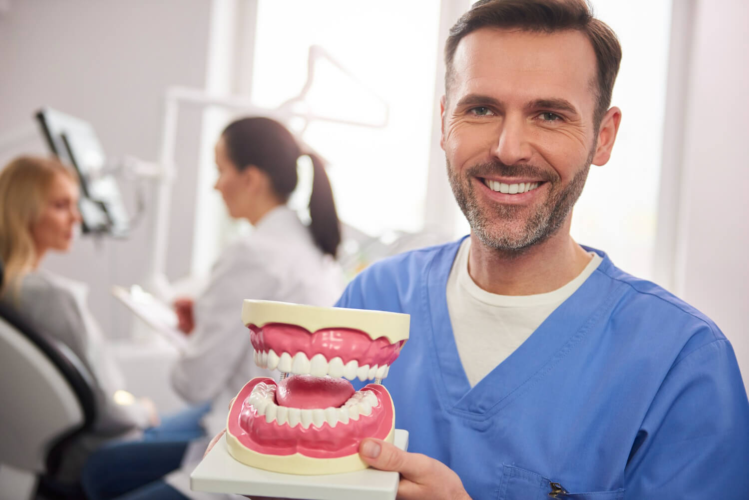 Dentista sorridente segura modelo didático de arcada dentária para explicar implante e prótese protocolo na Zona Leste de SP.