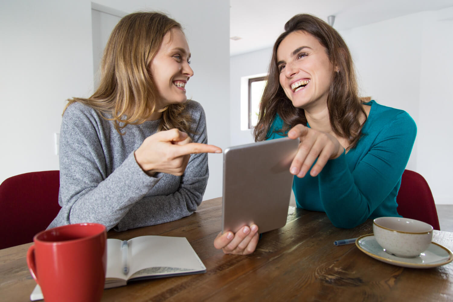 Duas mulheres sorriem ao olhar tablet, mostrando dentes claros. Saiba quando trocar lentes de contato dental na Zona Leste de SP.